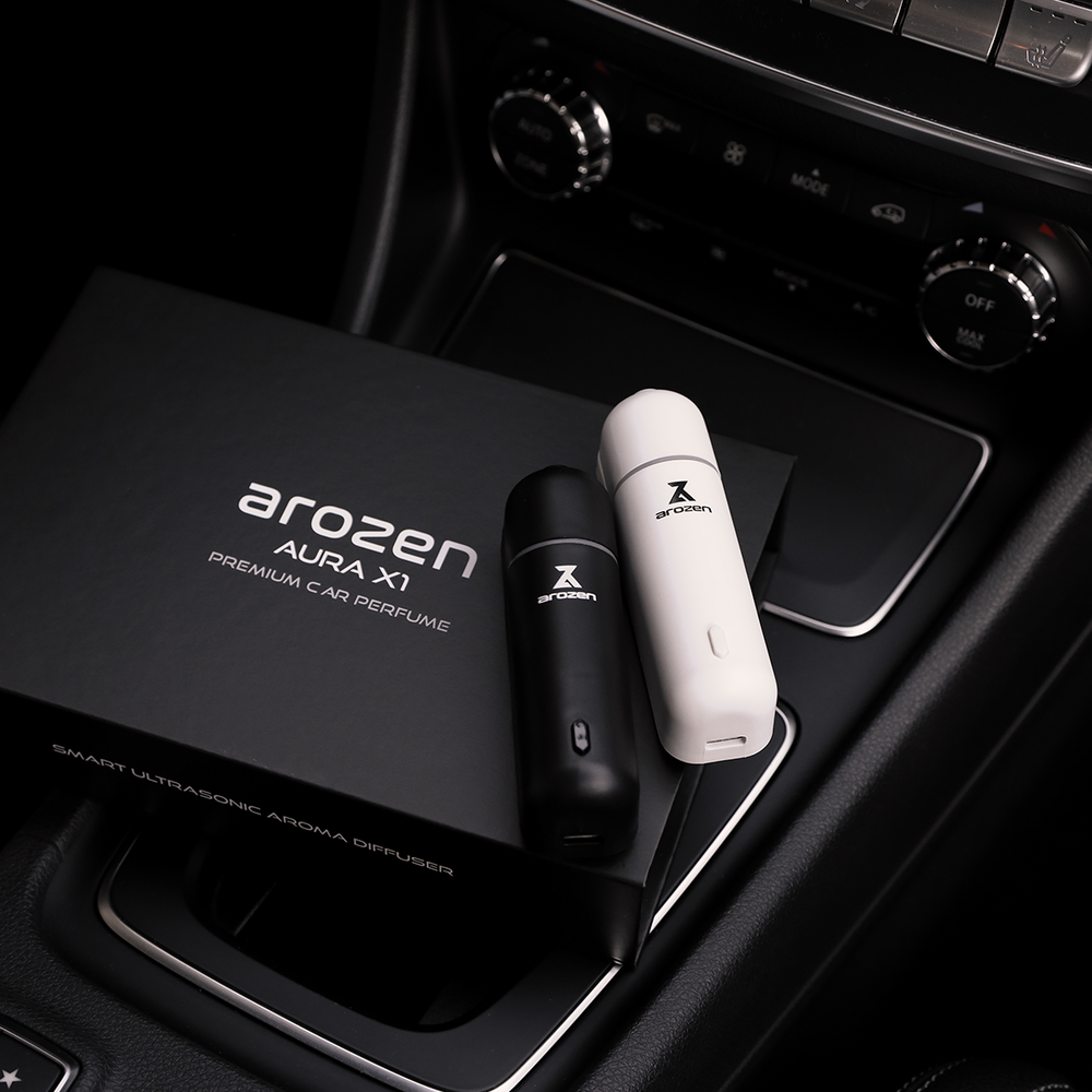 
                  
                    Two sleek AURA X1 CAR SCENT DIFFUSER units, one black and one white, rest on a car console beside the matching box labeled Premium Car Perfume, elevating your interior with luxurious fragrance oils.
                  
                