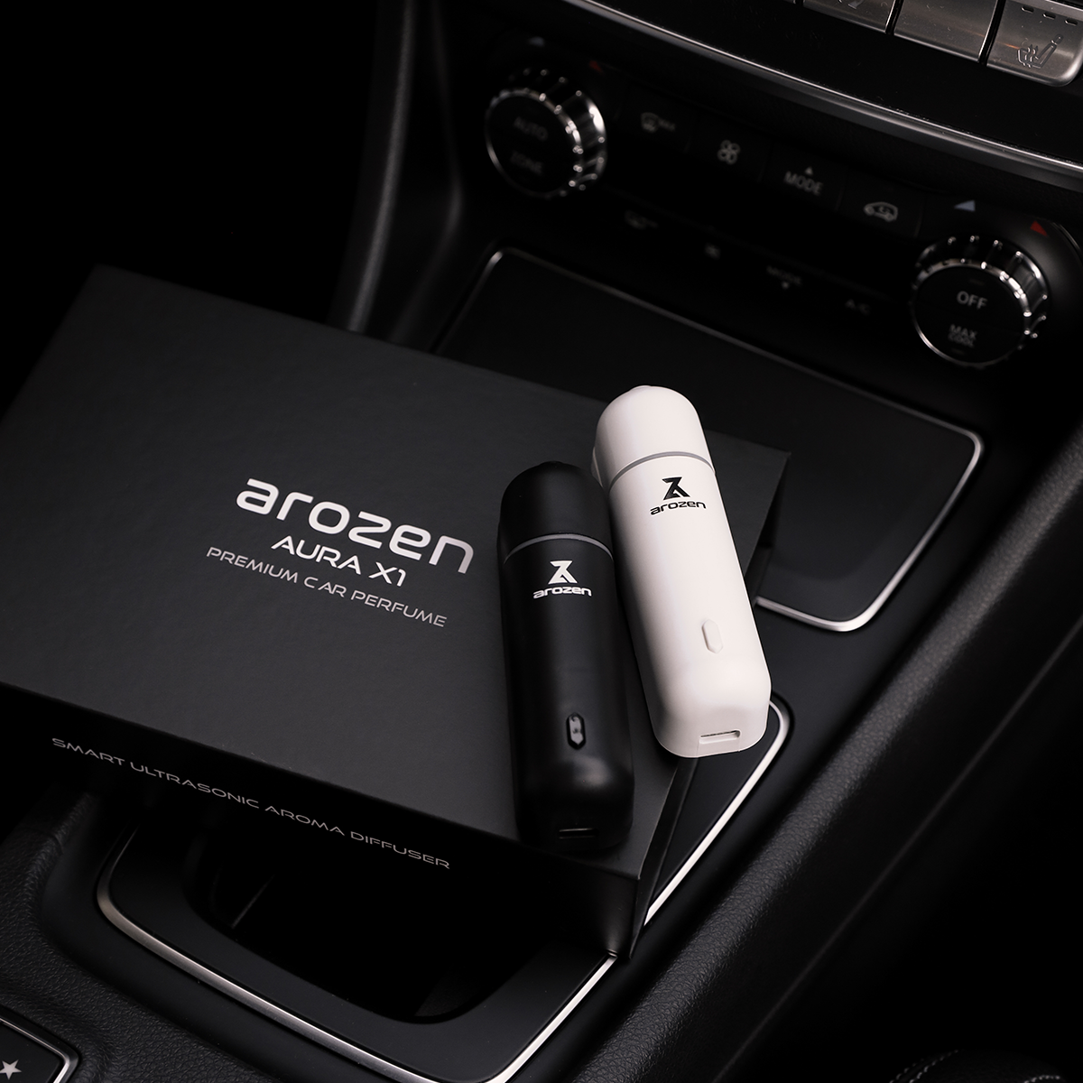 
                  
                    Two sleek AURA X1 CAR SCENT DIFFUSER units, one black and one white, rest on a car console beside the matching box labeled Premium Car Perfume, elevating your interior with luxurious fragrance oils.
                  
                