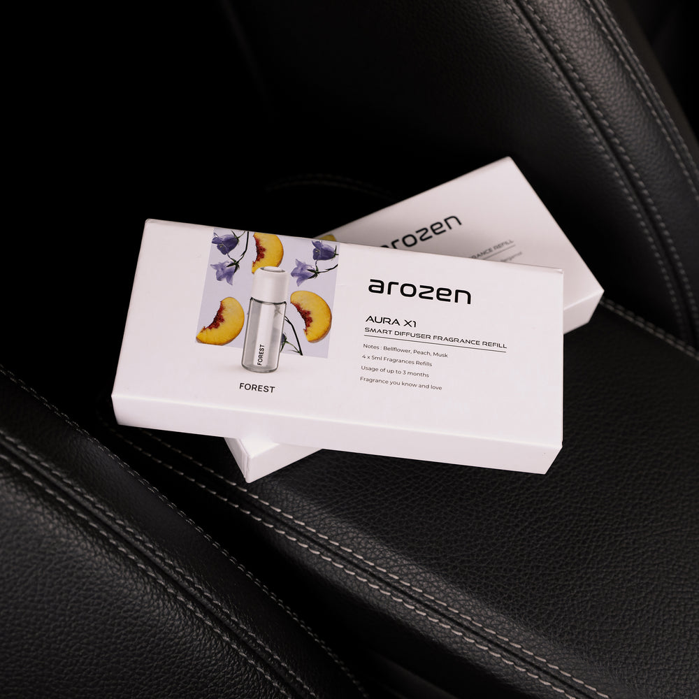 A box labeled Arozen WILD - AURA X1 FRGRANCE OIL REFILL, showing peaches and the diffuser, rests on a black leather car seat. Another WILD Car Scent Diffuser Oil box appears in the background, enhancing the luxurious atmosphere.