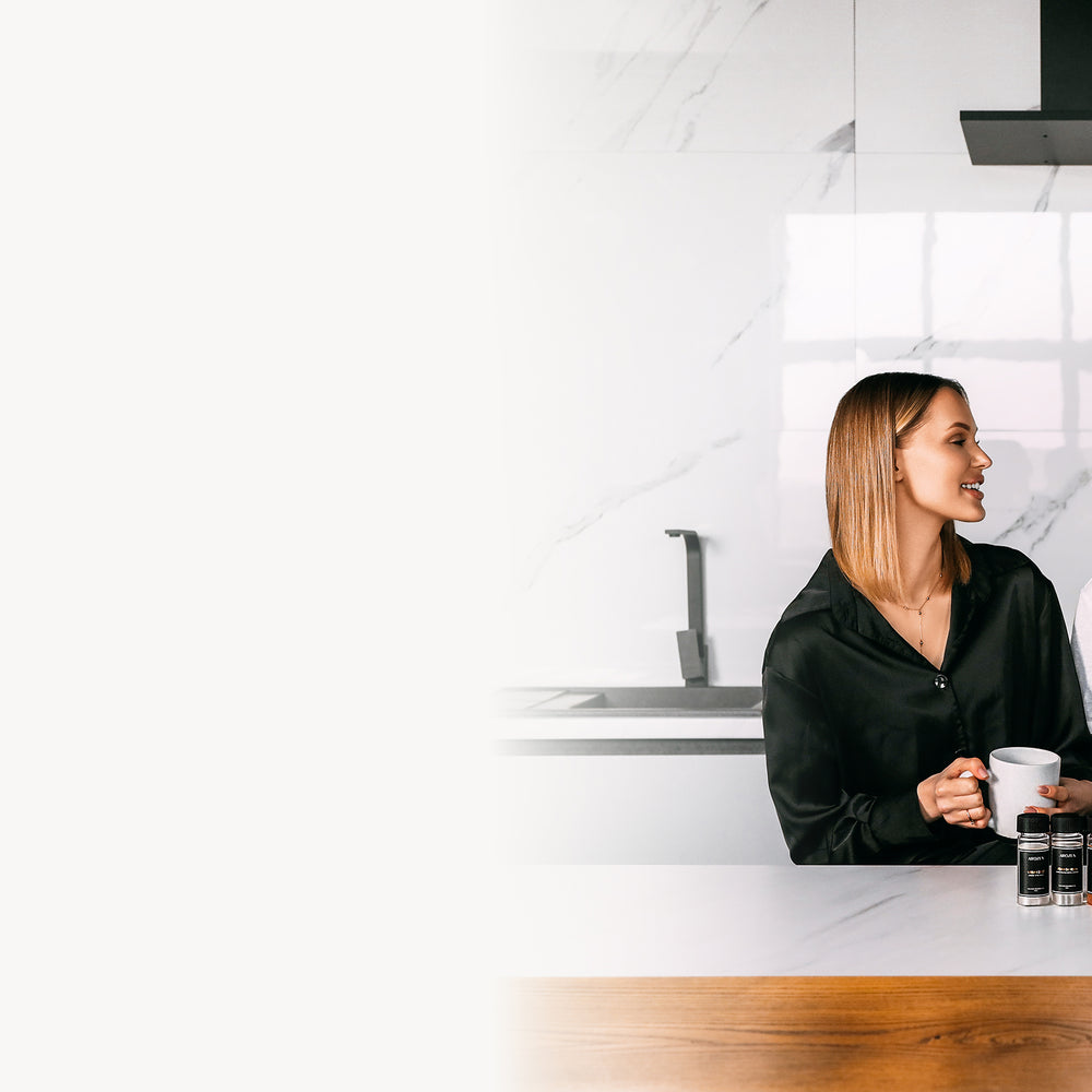 A woman and man sit at a modern kitchen counter with various electric scent diffuser products displayed in front of them. They are smiling at each other and appear relaxed, with a sleek kitchen backdrop and marble wall behind them.