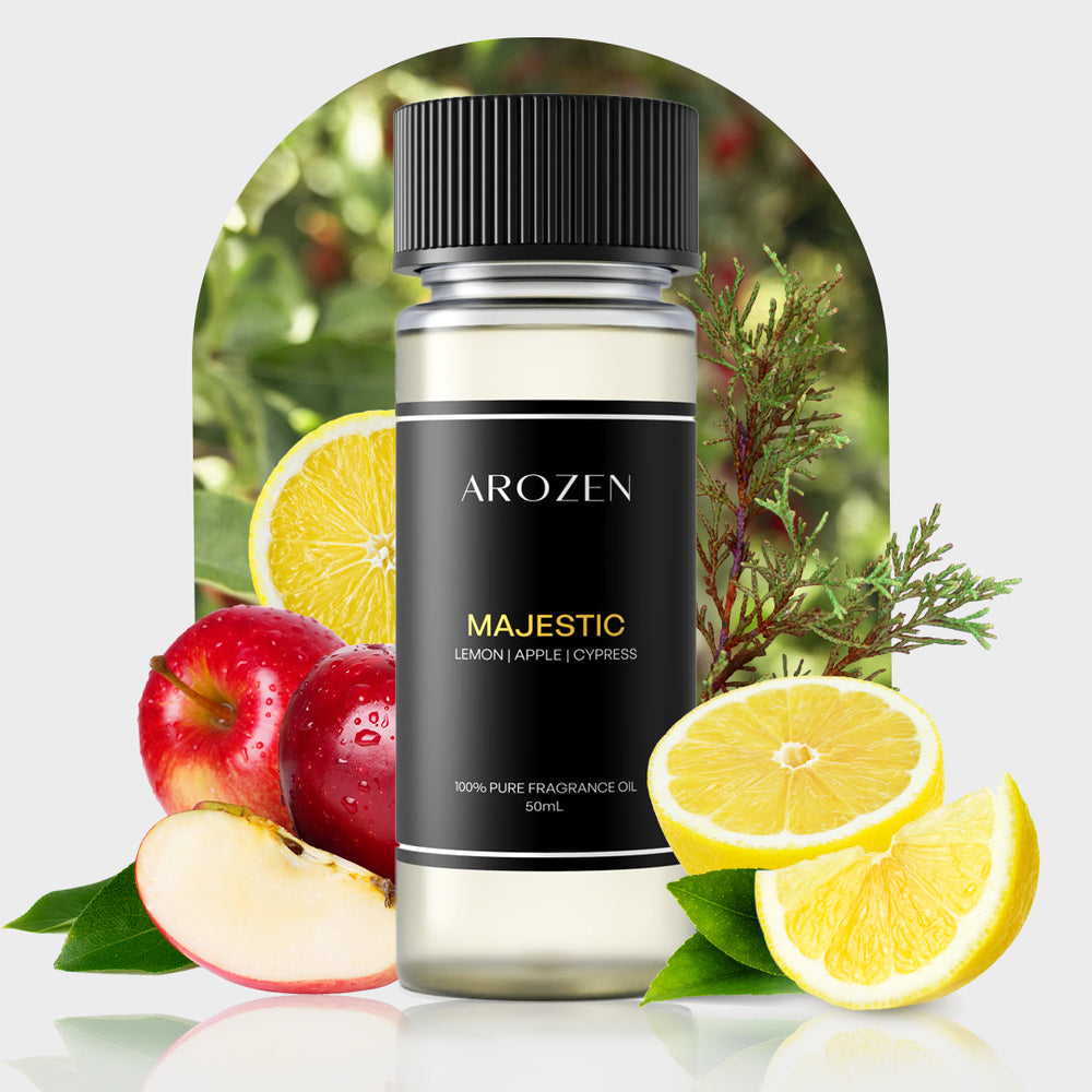 A bottle of Arozen MAJESTIC sits before apples, lemon slices, and cypress sprigs with a blurred garden behind. The label states: “Lemon | Apple | Cypress, 100% Pure Fragrance Oil, 50mL.”.